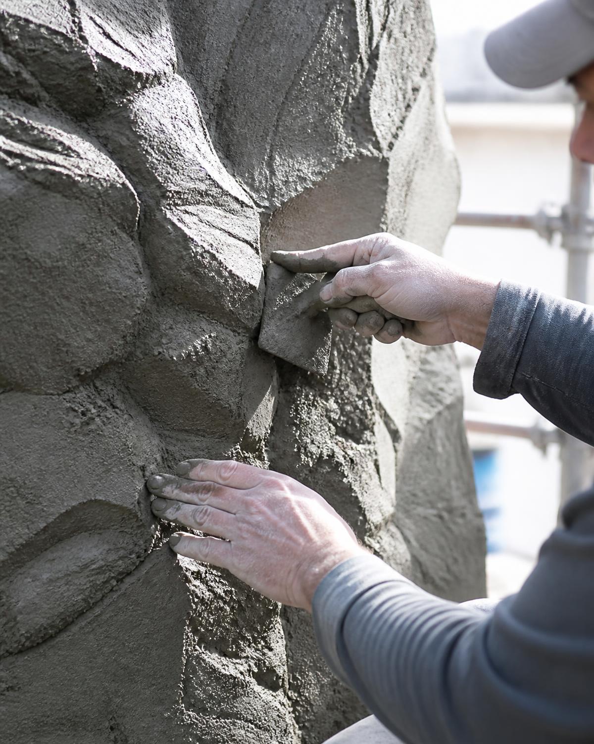 Sculptor carving wet shotcrete rock texture by hand on site